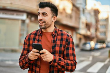 Genç İspanyol adam şehirde akıllı telefon kullanarak mutlu gülümsüyor..