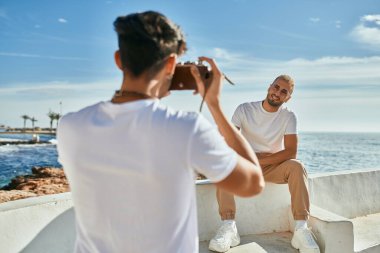 Denizin önünde erkek arkadaşının fotoğraflarını çeken bir adam..