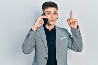 Kulakları genişlemiş genç beyaz bir çocuk akıllı telefondan konuşuyor bir fikir veya soruyla gülümsüyor ve mutlu bir yüzle işaret ediyor. 