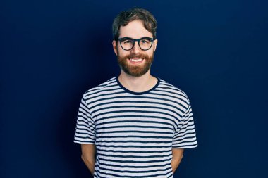 Sakallı, çizgili tişörtlü, gözlüklü mutlu ve havalı bir gülümsemesi olan beyaz bir adam. şanslı kişi. 