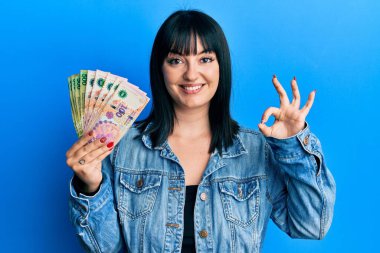 Arjantin Peso banknotları tutan genç İspanyol kadın parmaklarıyla imza atıyor, gülümseyerek mükemmel bir sembol oluşturuyor. 