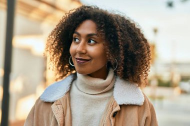 Genç Afrikalı Amerikalı kadın gülümseyerek şehirde mutlu mesut duruyor..