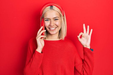 Güzel sarışın kadın akıllı telefonda konuşuyor parmaklarıyla imza atıyor, gülümsüyor ve mükemmel bir sembol oluşturuyor. 