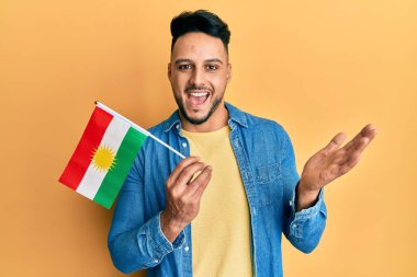 Kürdistan bayrağını tutan genç Arap adam başarıyı mutlu bir gülümsemeyle ve kazanan ifadeyle kutluyor. 