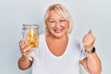 Orta yaşlı sarışın kadın elinde pişmemiş erişteyle gururla bağırıyor zaferi ve başarıyı kutluyor. 