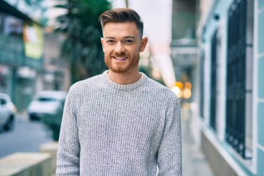 Genç beyaz adam gülümseyerek şehirde mutlu mesut duruyor..