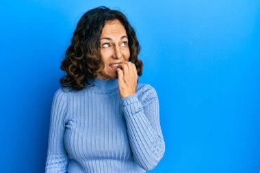 Orta yaşlı İspanyol kadın gündelik kıyafetler giyiyor. Stresli ve gergin görünüyor. Elleri ağızdan tırnak yiyor. anksiyete. 