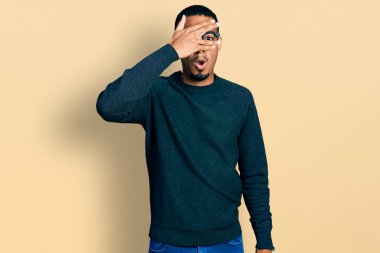 Genç Afro-Amerikan adam günlük giysiler ve gözlük takıyor. Şok olmuş bir şekilde yüzünü ve gözlerini kapatıyor. Utanmış bir ifadeyle parmaklarından bakıyor.. 