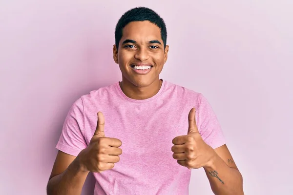 年轻英俊的他惊慌失措的男人穿着休闲的粉色T恤 成功的标志着用手做着积极的手势 竖起大拇指微笑着 快乐地 快乐的表达和胜利的姿态 — 图库照片