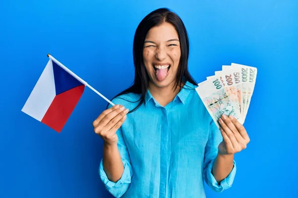 年轻的拉丁女人拿着切赫共和国国旗和可鲁纳钞票 带着滑稽的表情 伸出舌头 高兴极了 — 图库照片