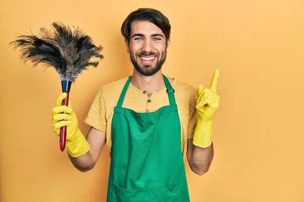 Joven Hombre Hispano Usando Delantal Sosteniendo Limpiador Plumero Sonriendo Feliz — Foto de Stock
