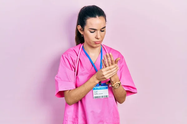 Young brunette woman wearing doctor uniform and stethoscope suffering pain on hands and fingers, arthritis inflammation
