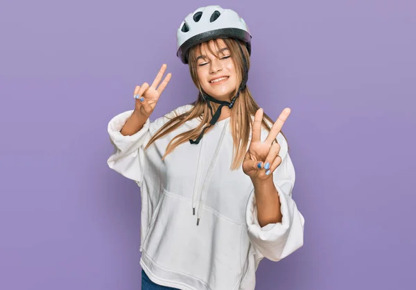 十几岁的女孩戴着自行车头盔 面带微笑地看着摄像机 手指在做胜利的标志 第二点 — 图库照片