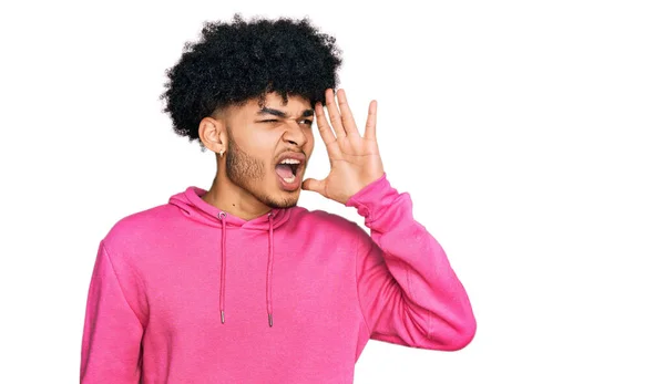 カジュアルなピンクのスウェットシャツを着たアフロの髪をした若いアフリカ系アメリカ人男性が大声で叫び 口の上で手で横に叫んでいます コミュニケーションの概念 — ストック写真