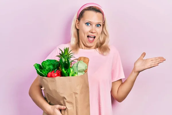 Beautiful Caucasian Blonde Woman Holding Paper Bag Groceries Celebrating Achievement — 스톡 사진