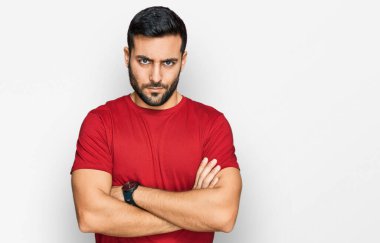 Gündelik kıyafetler giyen, kuşkucu ve gergin genç İspanyol bir adam. Yüzünde çapraz kollarla onaylamayan bir ifade var. negatif kişi. 