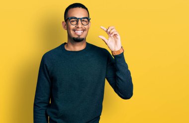 Sıradan kıyafetler ve gözlük takan, gülümseyen, kendine güvenen, el hareketi yapan, parmaklarıyla işaret yapan ve kameraya bakan Afro-Amerikan genç bir adam. ölçüm kavramı. 