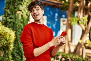 Genç İspanyol adam şehirde akıllı telefon kullanarak mutlu gülümsüyor..