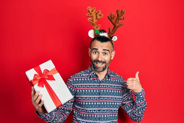 Ung Latinamerikan Man Bär Rådjur Jul Hatt Hålla Gåva Pekar — Stockfoto