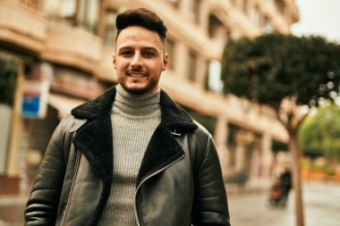 Genç Arap adam gülümsüyor, mutlu bir şekilde şehirde duruyor..