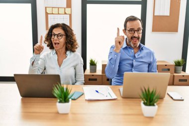 Orta yaşlı İspanyol bir kadın ve ofiste dizüstü bilgisayarı olan bir adam başarılı bir fikirle işaret ediyorlar. Heyecanlı ve mutlu. Bir numara.. 