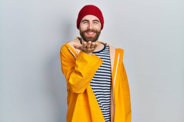 Sakallı, sarı yağmurluk giymiş beyaz bir adam kameraya bakıp havada el sallayarak öpüşüyor ve güzel ve seksi oluyor. aşk ifadesi. 