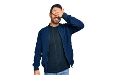 Gündelik kıyafetler giyen, gülümseyen ve gülümseyen genç İspanyol adam şaşırmak için gözlerini kapatıyor. kör kavram. 