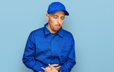 Kel ve sakallı bir adam midesi üstünde işçi tulumu giyiyor. Çünkü hazımsızlık, acı verici bir hastalık ve kendini iyi hissetmiyor. Ağrı kavramı. 