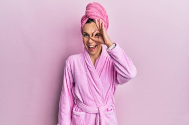 Duş başlığı ve bornoz takan genç sarışın kadın el hareketleriyle gülümsüyor ve mutlu yüzüyle parmaklarının arasından bakıyor.. 