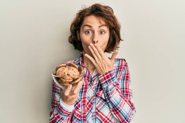 Elinde çikolatalı kurabiyeler tutan genç esmer kadın ağızlarını eliyle kapatıyor, şokta ve hata yapmaktan korkuyor. şaşırmış ifade 