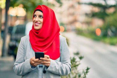 Şehirde akıllı telefon kullanan tesettürlü genç Arap iş kadını..