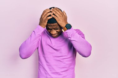 Genç siyah adam günlük pembe kazak giyiyor. Baş ağrısı, çaresiz ve stresli. Çünkü acı ve migren ağrısı var. Eller başının üstünde.. 