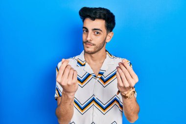 Gündelik kıyafetler giyen genç İspanyol adam elleriyle para hareketi yapıyor, maaş istiyor, milyonerlik işi yapıyor. 