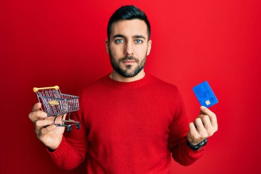 Küçük bir süpermarket arabası ve kredi kartı tutan İspanyol bir adam. Yüzünde ciddi bir ifadeyle rahatlamış. Basit ve doğal bir şekilde kameraya bakıyorsun.. 