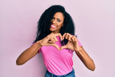 Orta yaşlı Afro-Amerikalı kadın, sıradan kıyafetler giyip, aşık gülümsüyor, elleriyle kalp sembolü yapıyor. romantik kavram. 