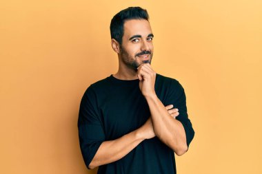 Gündelik giysiler giyen genç İspanyol adam kameraya kollarını kavuşturup çenesine dokunarak gülümsüyor. Olumlu düşünmek. 