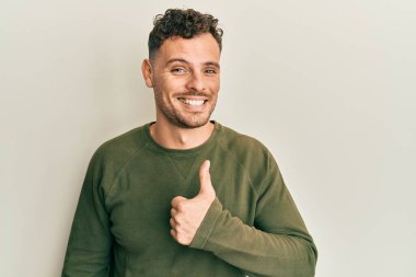 Gündelik kıyafetler giyen genç İspanyol adam elleriyle mutlu bir jest yapıyor. Kameraya bakıp başarıyı gösteren ifade. 