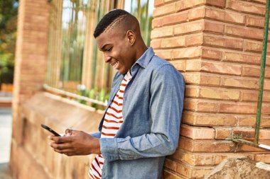 Genç Afrikalı Amerikalı adam şehirde akıllı telefon kullanarak mutlu bir şekilde gülümsüyor..