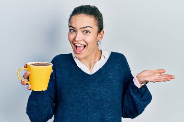 Kafkasyalı genç bir kız elinde kahveyle başarıyı mutlu bir gülümsemeyle kutluyor ve kazanan el kaldırarak ifade ediyor. 