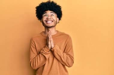 Afro saçlı, sıradan bir kazak giyen, elleri bağlı yalvaran ve dua eden, yüzünde umut ifadesi olan, duygusal ve endişeli genç bir Afro-Amerikalı. Yalvarıyor. 