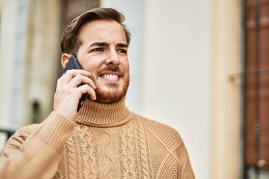 Genç beyaz adam gülümsüyor. Şehirdeki akıllı telefondan konuşuyor..