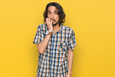 Günlük kıyafetler giyen genç İspanyol adam gergin ve gergin görünüyor. Ağzı tırnak yiyen eller. anksiyete. 