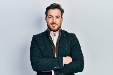 Yüzünde mutlu ve havalı bir gülümsemeyle kollarını kavuşturup gülümseyen sakallı yakışıklı beyaz bir adam. diş gösterme. 