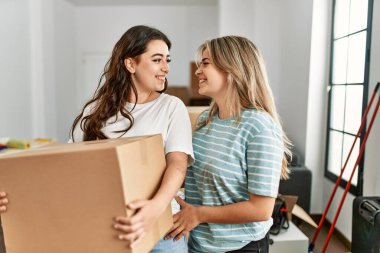 Genç ve güzel bir çift mutlu bir şekilde gülümsüyor. Yeni evlerinde karton kutu tutuyorlar..