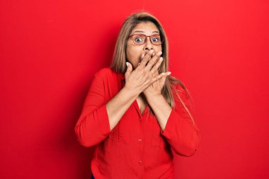 Orta yaşlı İspanyol kadın gündelik kıyafetler ve gözlük takıyor ağzı yanlışlıkla ellerle kapatıyor. gizli kavram. 