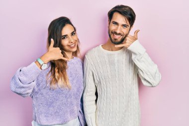 Genç İspanyol çift, günlük kıyafetler giyip gülümsüyor telefonla el ve parmaklarıyla jest yapıyor telefonda konuşuyor gibi. iletişim kavramları. 