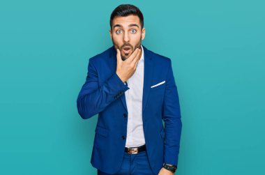 İş ceketi giyen genç İspanyol adam, elleri çenesinde, inanamama, şaşkınlık ve şaşkınlık dolu bir ifade takınıyor. 