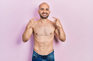 Tişörtsüz, güler yüzlü, parmaklarıyla ve ağzıyla gülümseyen genç kel adam. diş sağlığı kavramı. 