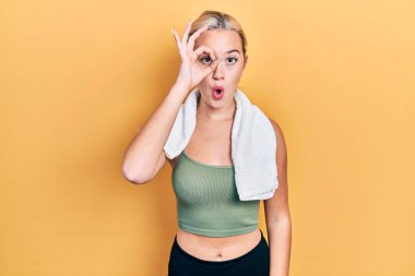 Spor kıyafetleri ve havlu giyen genç sarışın kız şaşırmış yüz ifadesiyle şaşırmış ve parmaklarından içeri bakıyor. İnançsız ifade. 