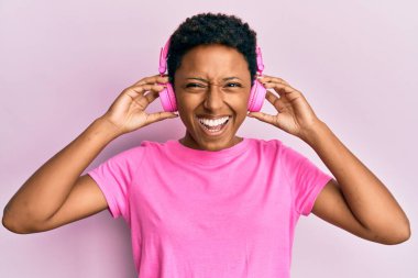 Genç Afrikalı Amerikalı kız kulaklıkla müzik dinliyor ve kahkahalarla gülüyor.. 